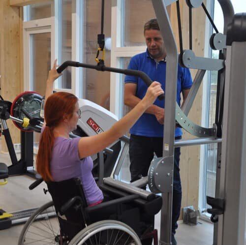 Kvinde i kørestol træner rygøvelser ved de nye maskiner.